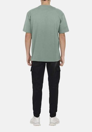 T-shirt oversized vert menthe à manches courtes, associé à un pantalon cargo noir avec poches latérales et poignets élastiques, porté avec des baskets blanches.