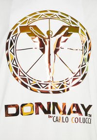 Tela blanca con un diseño de logo metálico en oro y cobre. Figura central con los brazos extendidos, rodeada de patrones geométricos y texto.