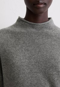 Grauer Pullover mit hohem Kragen, gefertigt aus weichem, strukturiertem Stoff. Das Design verfügt über eine einfache, klassische Form ohne Verzierungen.