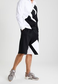 Black and white color-blocked shorts with geometric patterns. Made from soft fabric, featuring a relaxed fit and side pockets.