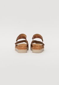 Brown leather sandals with padded straps and cork-wrapped wedge. Features a light-colored rubber sole and adjustable buckle closure.