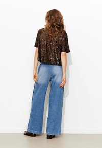 Top court en sequins marron assorti à un jean en denim bleu clair à jambes larges, avec une taille haute et une coupe décontractée. Des chaussures noires complètent le look.