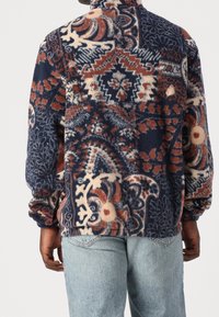 Pile con collo alto, caratterizzato da un motivo astratto multicolore in blu, arancione e crema. Polsini e orlo a coste.