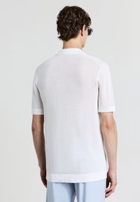 Weißes Kurzarmhemd mit strukturiertem Mesh-Design, ausgestattet mit einem flachen Kragen, gerippten Bündchen und einem geraden Saum.