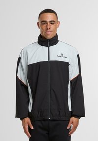 Juoda ir šviesiai mėlyna zip-up striukė su aukštu apykakle, elastingomis rankogaliais ir apvadu; kūno dalyje yra logotipas ir oranžiniai akcentai.