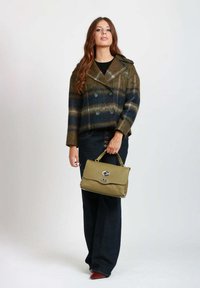 Cappotto doppiopetto in lana a quadri nei toni del verde e blu, abbinato a jeans scuri a vita alta e una borsa oliva con dettagli in argento.