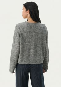 Pull en maille grise avec un col rond, des épaules tombantes et un ourlet côtelé. Texture douce et coupe décontractée, associé à un pantalon rayé bleu marine.