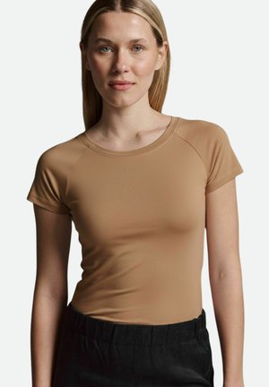 Beige eng anliegendes T-Shirt mit kurzenÄrmeln und Rundhalsausschnitt, aus einem glatten, dehnbaren Stoff. Tragen mit schwarzen, hoch taillierten Hosen.