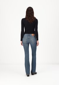 Top de manga larga oscuro combinado con unos vaqueros acampanados de un azul claro. Los vaqueros tienen un detalle de costura y una etiqueta en el bolsillo trasero. Textura suave.