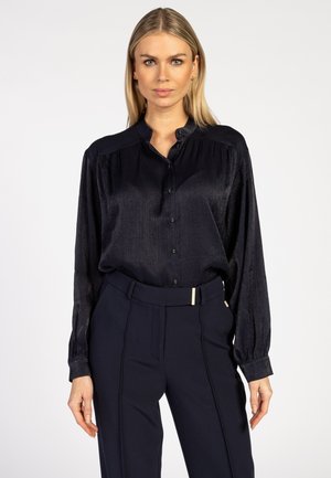 Marineblauwe blouse met lange mouwen, een subtiele glans, knoopsluiting aan de voorkant, pinstrepen op de schouders en een ronde halslijn.
