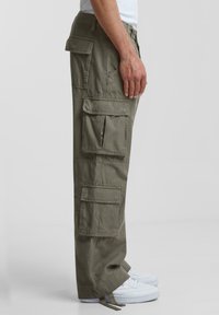Pantaloni cargo de culoare verde măslinie cu multiple buzunare, croi drept, din material de bumbac, cu tivuri răsucite și șnur la baza pantalonului.