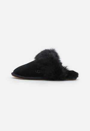 Chausson noir à enfiler avec une doublure en fourrure douce et un extérieur en daim, doté d'un petit talon et d'une semelle souple.