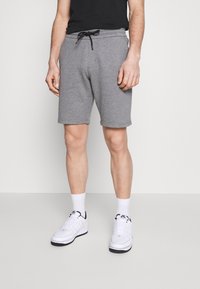 Shorts gris en mélange de coton avec une ceinture élastique et un cordon de serrage, dotés de deux poches latérales et d'une coupe décontractée, associés à des baskets blanches.