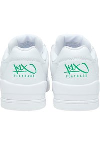 Fehér sportcipők sima bőr felsőrészel, texturált díszítésekkel és zöld nyomtatott "K1X PLAYHARD" logóval a sarokrészen. Gumi talp, alacsony szárú kialakítás.