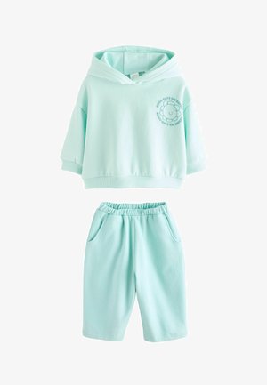 Sweat à capuche en coton vert menthe avec une coupe courte, orné d'un logo de fleur brodé. Accompagné d'un short assorti vert menthe avec poches.