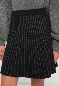 Jupe noire avec des rayures verticales ondulées argentées. Matériel tricoté, ceinture élastique, et ourlet évasé. Texturée avec une apparence côtelée.