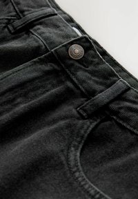 Černé džíny z denimu s kovovým knoflíkem, poutky na opasek a detailním pohledem na texturu látky a švy.
