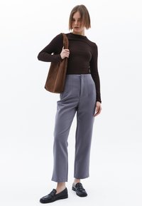 Brun långärmad tröja i kombination med grå högmidjade byxor. Modellen håller en brun mocka tote-väska och bär svarta loafers. En enkel, skräddarsydd design.