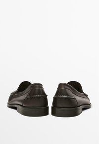 Dark brown leather shoes with a smooth finish, featuring a low heel and decorative stitching on the back. Minimalist design with no embellishments.