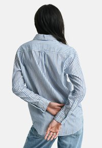 Gestreept overhemd in lichtblauw en wit, lange mouwen, ontspannen pasvorm, met een achter-yoke en een gebogen zoom. Het materiaal lijkt lichtgewicht.