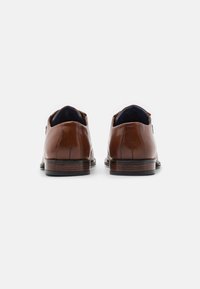 Zapatos de vestir de cuero marrón con punta redondeada, textura suave, costuras sutiles y tacón de madera. Detalle de cremallera en el lateral.