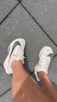 Benen in witte Nike Zoom Fly hardloopschoenen op een grijze tegelvloer.