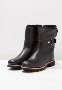 Botas de cuero negro hasta el tobillo con forro de piel sintética, detalle de hebilla lateral, punta redonda y suelas de goma texturizadas para mayor agarre.