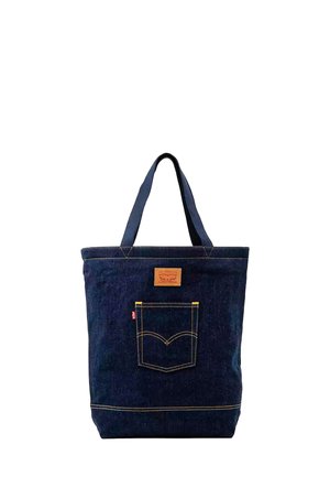 Bolso tote de denim azul oscuro con doble asa, bolsillo frontal con costuras amarillas y un parche de cuero marrón sobre el bolsillo.