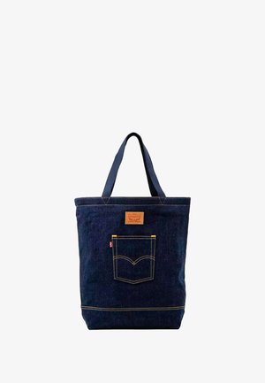 Bolso tote de denim azul oscuro con doble asa, bolsillo frontal con costuras amarillas y un parche de cuero marrón sobre el bolsillo.