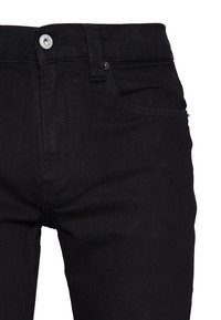 Jeans de mezclilla negra con un diseño estándar de cinco bolsillos, cierre con botón metálico y una textura suave con desvanecimiento mínimo.