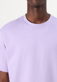 Camiseta de algodón lila con cuello redondo y mangas cortas. Textura suave y diseño sencillo, sin patrones ni acentos.