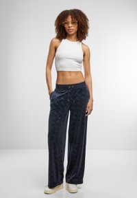 Navy velvet wide-leg pants with an embossed logo pattern, elastic waistband, and drawstring. Paired with a fitted white crop top.