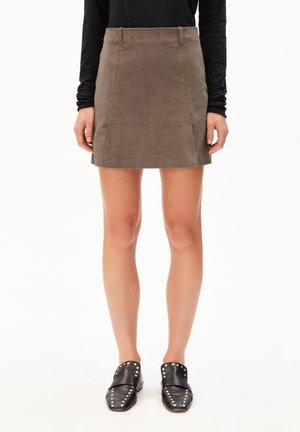 Khaki corduroy mini-jurk met een rechte silhouet, voorzakken en subtiele gestikte details. Gecombineerd met zwarte loafers met studs.