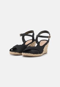 Sandales compensées noires avec brides croisées, dessus en tissu, semelle en jute style espadrille et bride autour de la cheville avec boucle dorée.