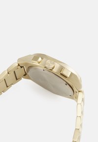 Goldfarbener Metallarmbanduhr mit rundem Gehäuse, strukturiertem Lünette, Drückern und einem Gliederarmband. Klarglas bedeckt das Ziffernblatt.