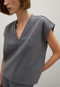 Graues, kurzärmliges Oberteil aus einem weichen, strukturierten Stoff mit V-Ausschnitt und sichtbaren Schulternähten. Schlichtes, minimalistisches Design.