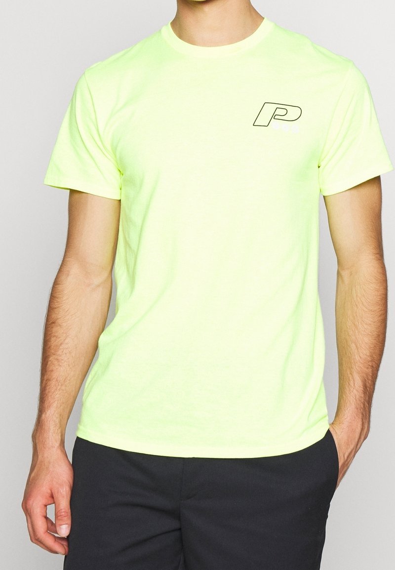 Neonově žluté bavlněné tričko s kulatým výstřihem a krátkými rukávy, se černým logem "P" na levé části hrudi. Hladká textura.
