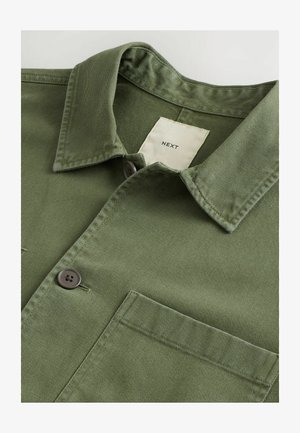 Oliwkowa bawełniana koszula z kołnierzykiem rozłożonym, dwiema brązowymi guzikami i kieszenią na piersi. Posiada teksturowany materiał oraz wewnętrzną metkę.