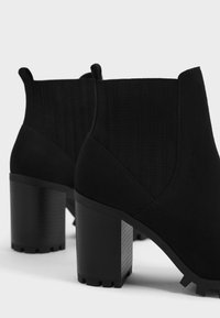 Black suede ankle boots featuring a block heel, ribbed accents, and a textured outsole. Designed with a clean, modern silhouette.