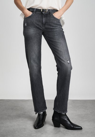Jeans in denim grigio scuro con taglio dritto, dettagli strappati sulle ginocchia e orli sfrangiati, abbinati a stivali neri con punta a punta.