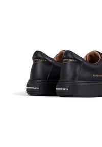 Sneaker in pelle nera con suola spessa, con marchio oro e nero sul tallone e superficie liscia. Design arrotondato con dettagli minimali.