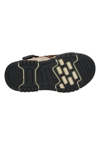 Zwarte rubberen zool met textuur voor grip, witte accenten en een patronenprofiel. Beschikt over een klittenbandsluiting op een bruin bovenstuk.