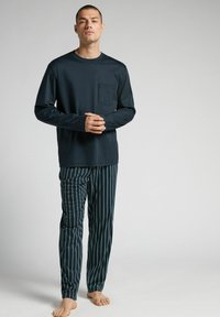 Langärmeliges, dunkelblaues Oberteil mit einer Brusttasche, kombiniert mit gestreiften Schlafanzughosen in Dunkelblau und Teal. Weicher Stoff mit entspannter Passform.