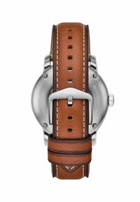 Bracelet de montre en cuir marron avec des accessoires en argent. Ses caractéristiques incluent des coutures décoratives et un cadran rond avec le nom de la marque.