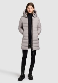 Light gray puffer coat with a hood, featuring a quilted design, side pockets, and a mid-length cut. Worn over a black top and leggings.