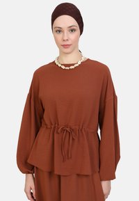 Brown lightweight top with long sleeves, cinched waist, and textured fabric. Accentuated by a tie detail and paired with a matching bottom.