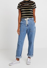 Czarna koszulka w paski z żółtymi i białymi liniami, dżinsy z wysokim stanem i kieszeniami naszytymi, zakończenie z wywinięciem, białe trampki.