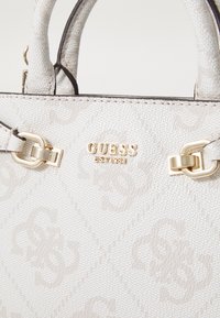 White textured handbag with embossed patterns, gold hardware, and logo detail. Features dual handles and a structured shape.
