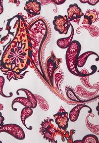 Tessuto bianco con intricati motivi paisley in rosso, arancione e viola scuro, con dettagli floreali e forme ondulate in tutto il design.