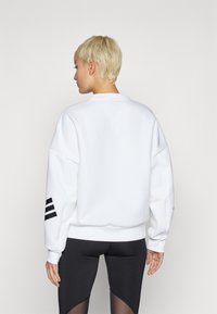 Hvitt sweatshirt med rund hals og senket skuldre. Har tre svarte striper på venstre erme og en avslappet passform.